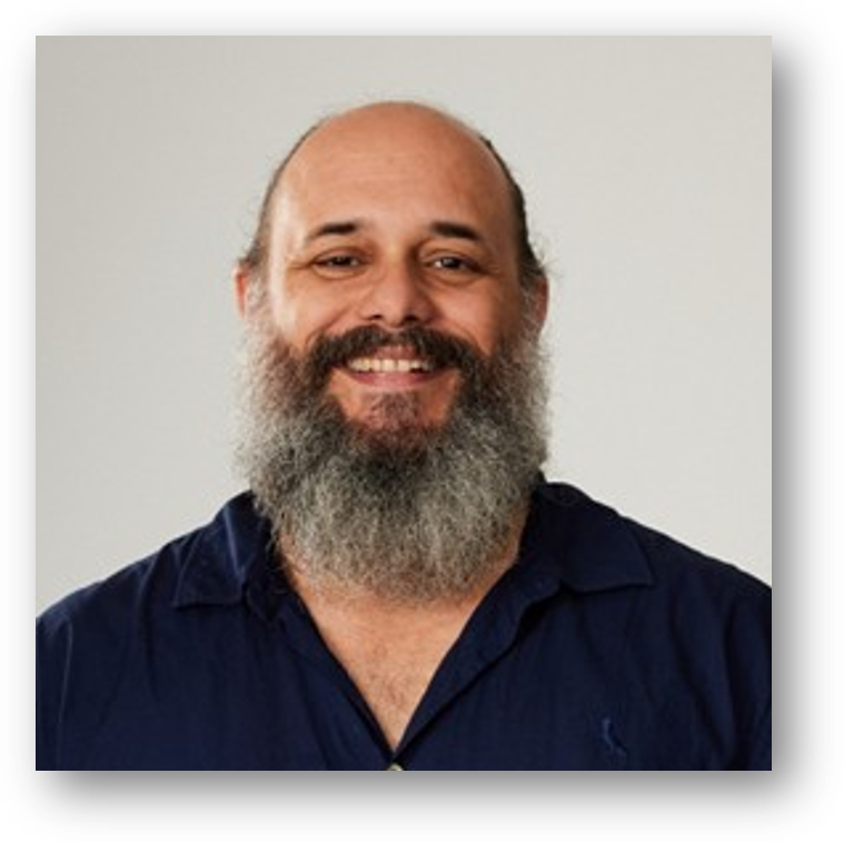 Fernando Dineli, sorrindo, com barba grisalha e camisa azul